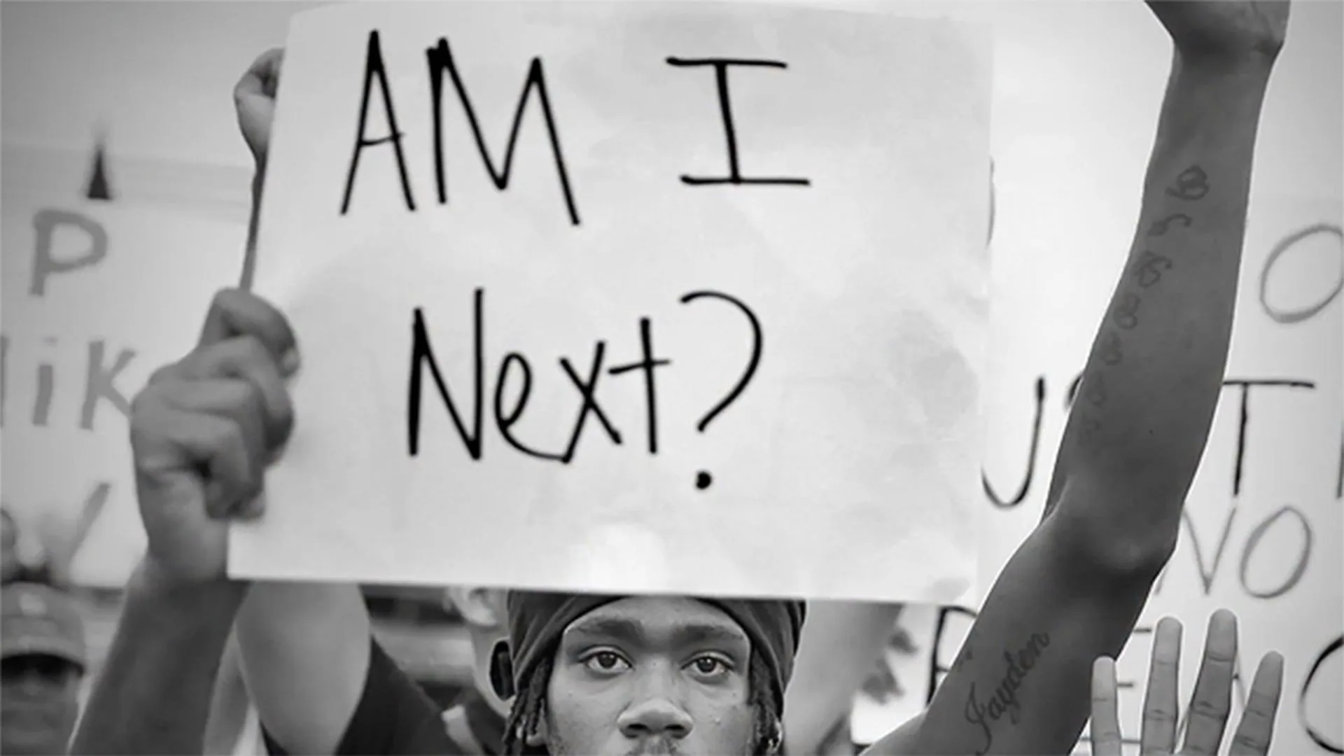 Cena de a 13ª emenda, rapaz negro segurando cartaz "Eu sou o próximo?" em protesto.
