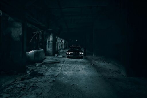 Carro estacionado em um galpão escuro, iluminado pelos faróis, em uma atmosfera cinematográfica