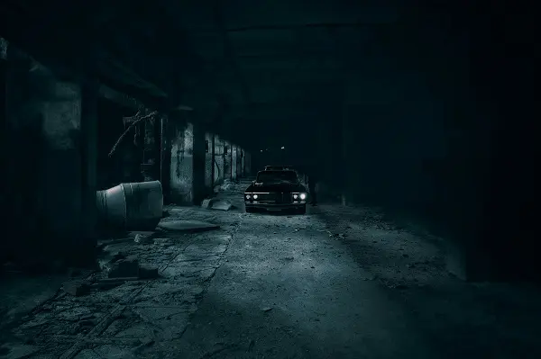 Carro estacionado em um galpão escuro, iluminado pelos faróis, em uma atmosfera cinematográfica